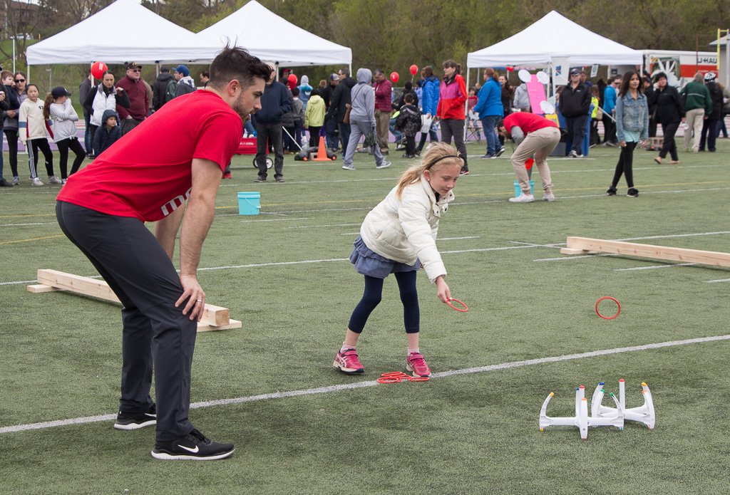 Girl performing a ring toss as part of obstacle course, with onlooking volunteer 