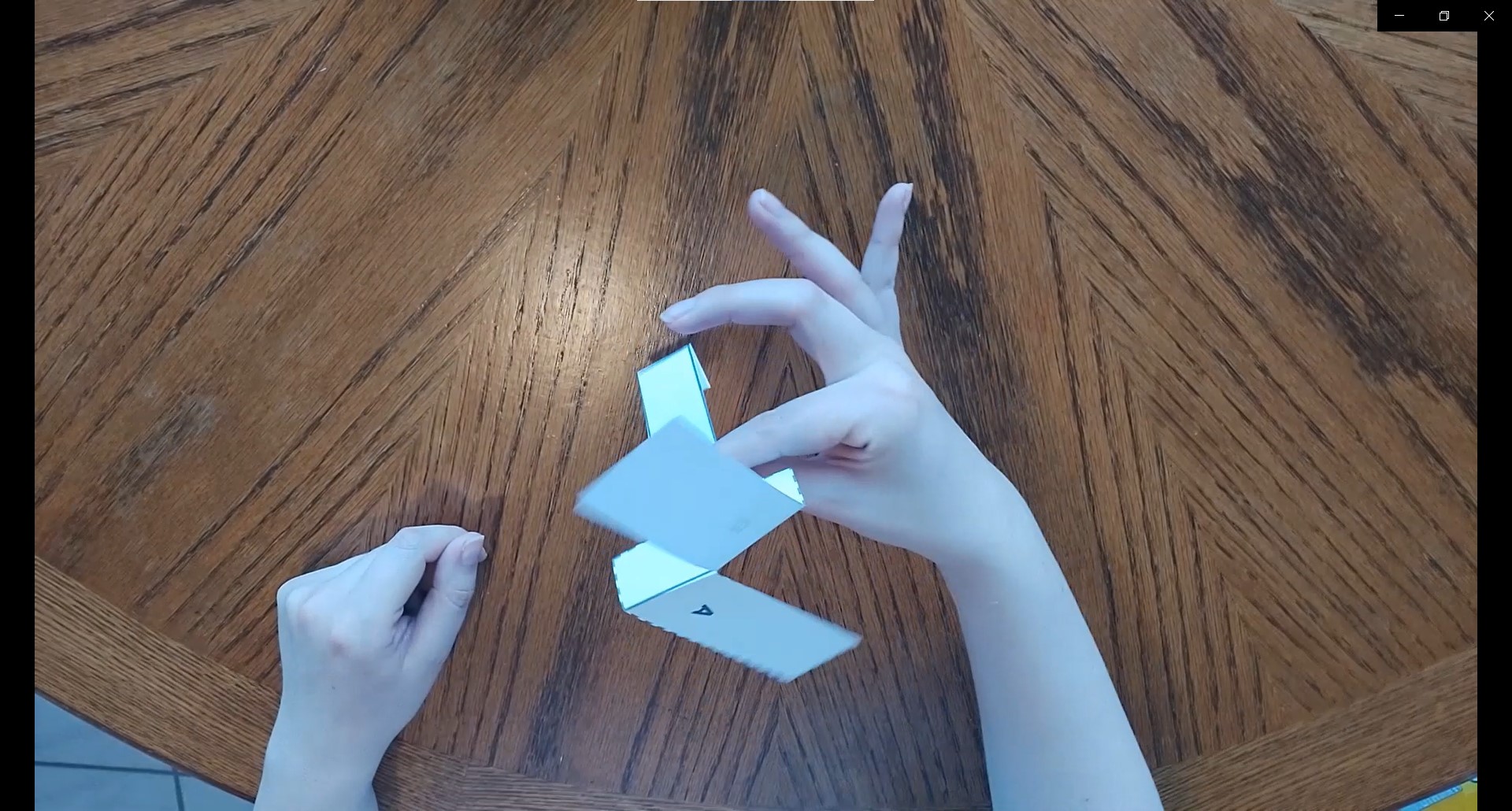 Paper helicopter being held between thumb and index held above a brown wood table 