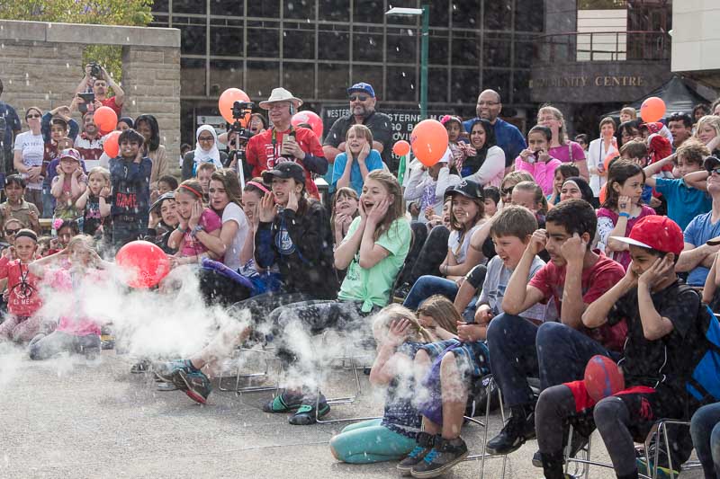 Smiling and cheering crowd watching science demonstration with smoke in the foreground 