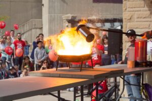 Scientific demonstration displaying growing flames with onlooking crowd in the background