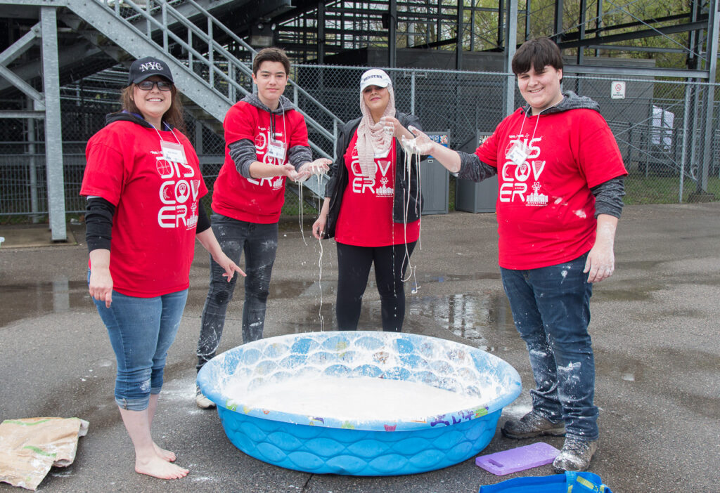 Four volunteers stand around baby pool filled with oobleck 